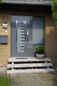Moderne Haustür in Grau mit Glaseinsatz und Treppe aus Naturstein vor einem Ziegelhaus.