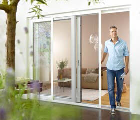 Mann öffnet große Schiebetür aus Glas und betritt modernen, hellen Wohnbereich.