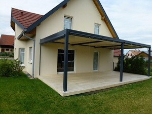 Moderne Terrassenüberdachung aus Metall an einem Einfamilienhaus mit gepflegtem Garten.