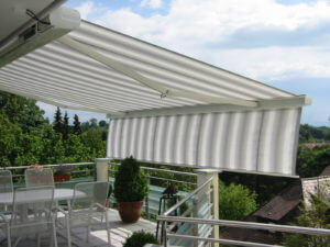 Moderne Markise spendet Schatten auf sonniger Terrasse mit Gartenmöbeln und Pflanzen.