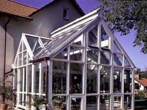 Moderner Wintergarten mit Glasdach und weißen Rahmen an einem Einfamilienhaus im Garten.